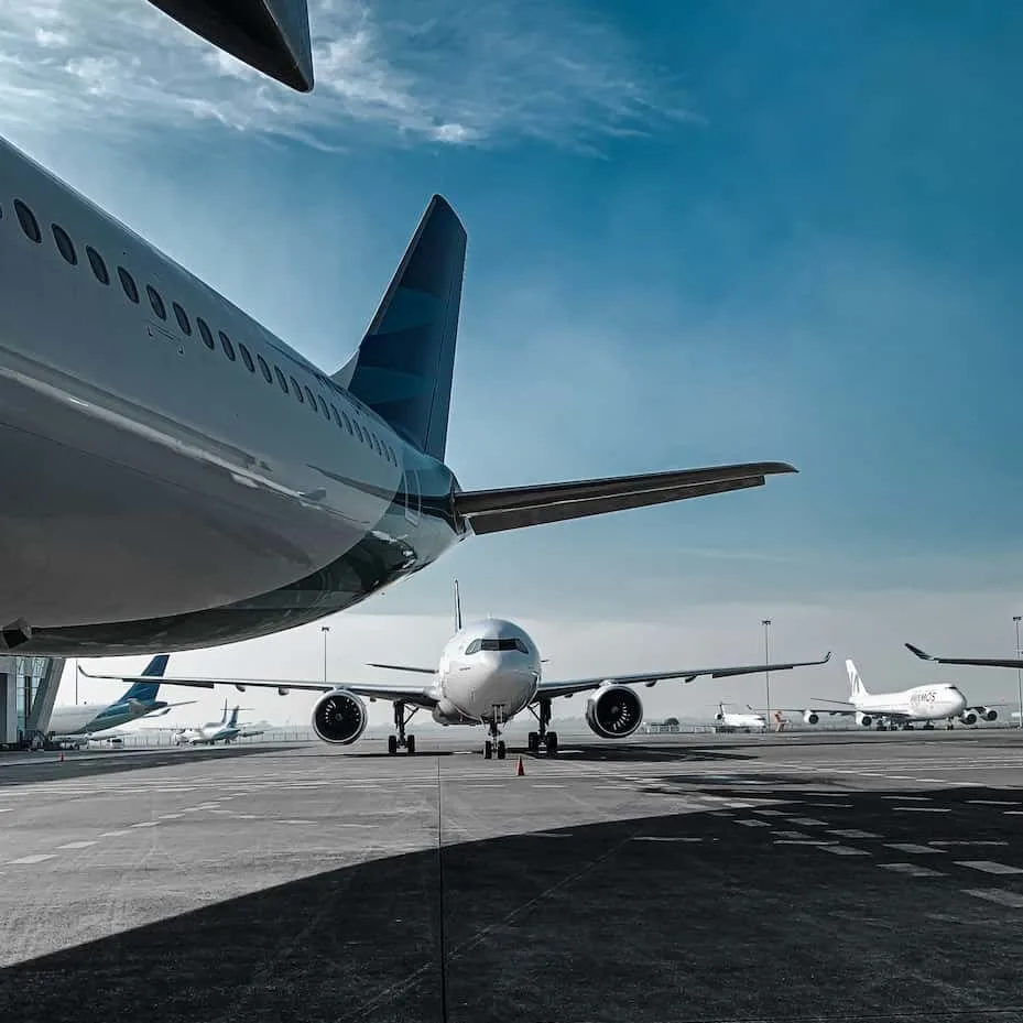 A view of an airport runway with multiple airplanes, showcasing a large aircraft in the foreground and several others in the background under a blue sky.